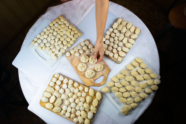 小麦粉で焼かれた女性の手は、きれいに手作りされ、新しく作られた餃子、ラビオリとキンカリをまな板の上にレイアウトします。おいしい自家製食品。白の背景、クローズアップ、選択的焦点、フラットレイ. - 写真・画像