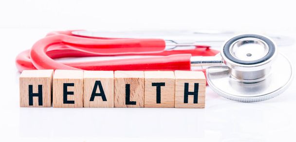Das Wort Gesundheit aus Holzbuchstaben neben einem Stethoskop auf weißem Hintergrund. - Foto, Bild