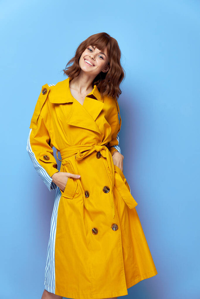 Mooie vrouw glimlachende handen in de zakken van een gele jas  - Foto, afbeelding