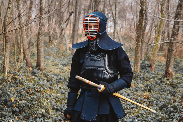 Человек, практикующий кэндо с бамбуковым мечом синай на фоне леса. Место для текста или рекламы. - Фото, изображение