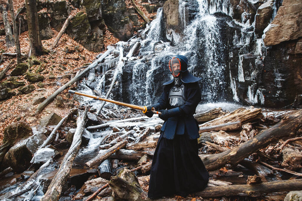De mens oefent kendo met bamboe zwaard op waterval, rotsen en bosachtergrond. Plaats voor tekst of reclame. - Foto, afbeelding