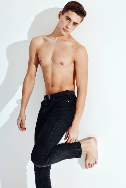 Handsome guy with a naked torso stands on one leg against the wall - 写真・画像