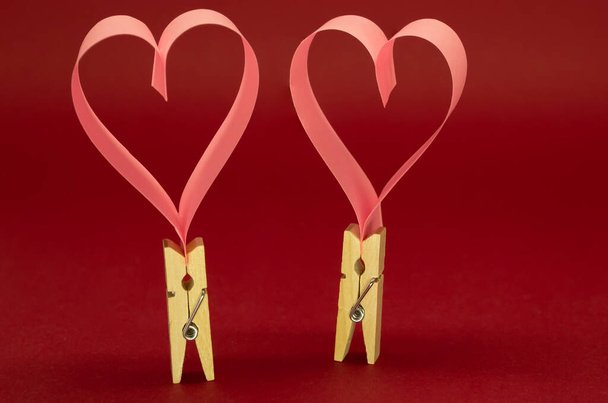 Das Konzept einer Liebesbeziehung, eines Paares. Wäscheklammern aus Holz mit Papierherzen auf rotem Hintergrund - Foto, Bild