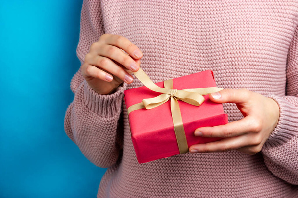 The girl on a blue background unties the ribbon on the gift box. - Photo, image