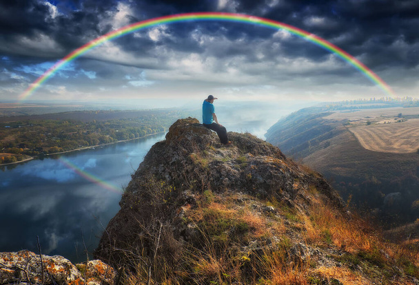 川の上にカラフルな虹。渓谷の上の岩の上の男 - 写真・画像