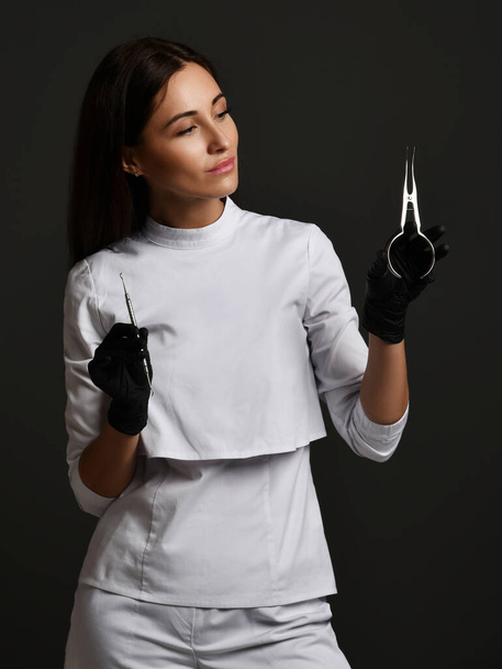 Young smiling woman doctor dentist in white uniform and latex gloves standing holding medical dental tools - Foto, Imagen