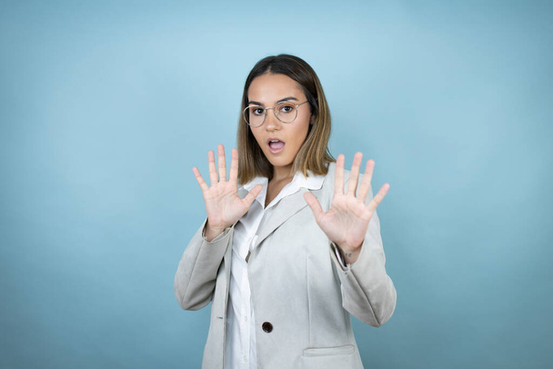 Young business woman over isolated blue background afraid and terrified with fear expression stop gesture with hands, shouting in shock. Panic concept. - Photo, Image