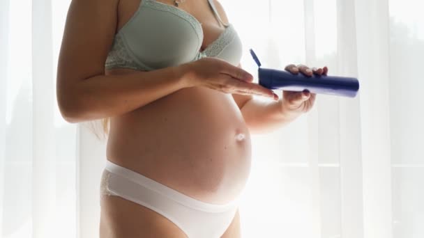 SIlhouette de mujer embarazada con gran vientre aplicando crema hidratante o loción para prevenir las estrías en la piel. Concepto de belleza, embarazo y salud. - Imágenes, Vídeo