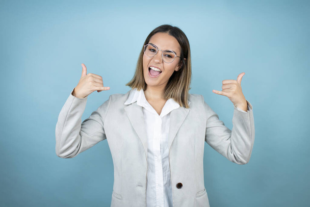Giovane donna d'affari su sfondo blu isolato gridando con espressione pazza facendo simbolo di roccia con le mani in alto - Foto, immagini