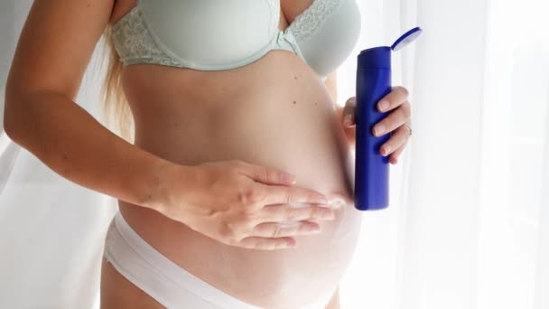 Lähikuva raskaana olevan naisen rintaliivit ja pikkuhousut soveltamalla creme hänen ruumiinsa ja huolehtii hänen ihonsa. Käsitys kauneus, raskaus ja ihonhoito. - Materiaali, video