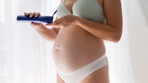 Zbliżenie młodej kobiety w ciąży w bieliźnie dbającej o skórę i stosującej krem nawilżający lub balsam. Pojęcie piękna, ciąży i pielęgnacji skóry. - Materiał filmowy, wideo