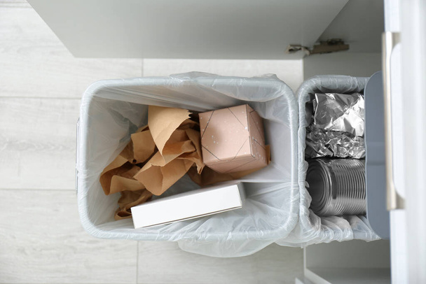 Open kast met volle vuilnisbakken voor gescheiden afvalinzameling in keuken, bovenaanzicht - Foto, afbeelding