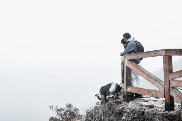 die Wanderer posieren am Rande eines nebligen Berges und der Schäferhund begleitet sie - Foto, Bild
