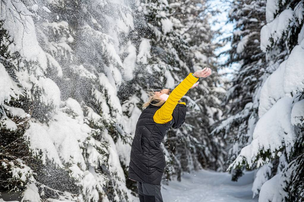 Ευτυχισμένη γυναίκα ρίχνει χιόνι σε μια όμορφη χειμωνιάτικη μέρα. - Φωτογραφία, εικόνα