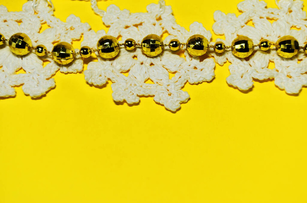 Three knitted white snowflakes with yellow shiny beads on the top edge on a yellow background with a copy space - Foto, afbeelding