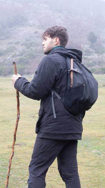 Der junge kaukasische Wanderer beginnt seine Route durch den Berg mit einem Stock. - Foto, Bild