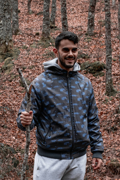 Το χαμογελαστό αγόρι κρατά ένα ραβδί ενώ περπατά στο δάσος του φθινοπώρου - Φωτογραφία, εικόνα
