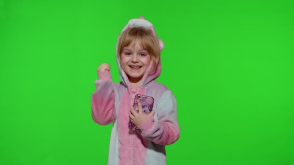 Podekscytowany dziewczynka w piżamie jednorożca za pomocą telefonu komórkowego, okazało się wielkie zwycięstwo wiadomości - Materiał filmowy, wideo
