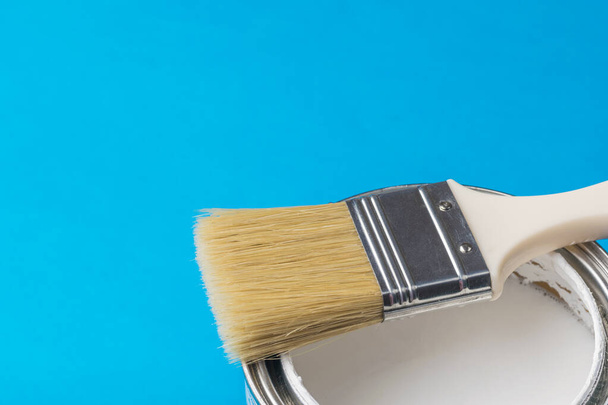 Pinsel mit langen Borsten auf einer offenen Farbdose auf blauem Hintergrund. Ausführung von Malerarbeiten. - Foto, Bild