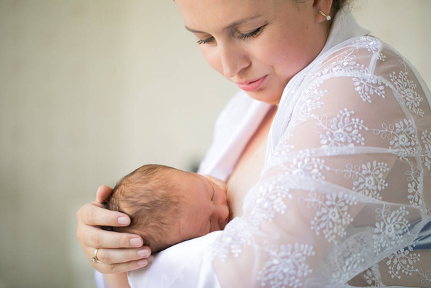 mom feeds newborn standing in a white interior. breast-feeding. - Photo, Image