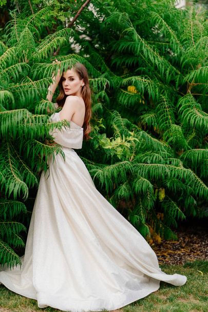 beautiful woman in a white dress posing in against of green leaves. - 写真・画像