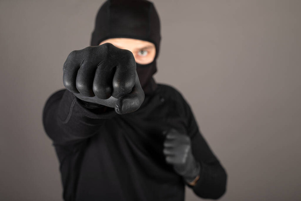 Dangereux coup de poing criminel vers la caméra, portant un masque noir et costume - Photo, image