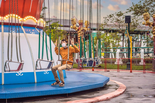Man riding a carousel wearing a medical mask during COVID-19 coronavirus - Foto, afbeelding
