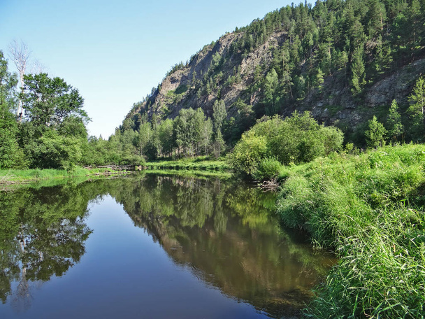 domb zöld fákkal és kék ég tükröződik a vízben, Olenyi Ruchyi park, Bazhukovo, Oroszország - Fotó, kép