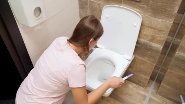 Mujer joven en pijama sintiéndose enferma vomitando en el inodoro después de hacer la prueba de embarazo. Intoxicación y náuseas durante el embarazo - Metraje, vídeo