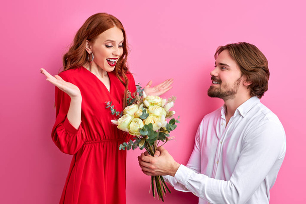 Romantik randevu: Kafkasyalı adam kızıl saçlı genç bayana çiçek sunuyor. - Fotoğraf, Görsel
