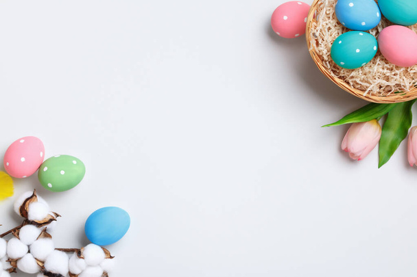 Happy easter. Multicolored eggs in a basket, tulips and a branch of cotton on a gray background. Flat lay greeting card copy space. - Foto, imagen