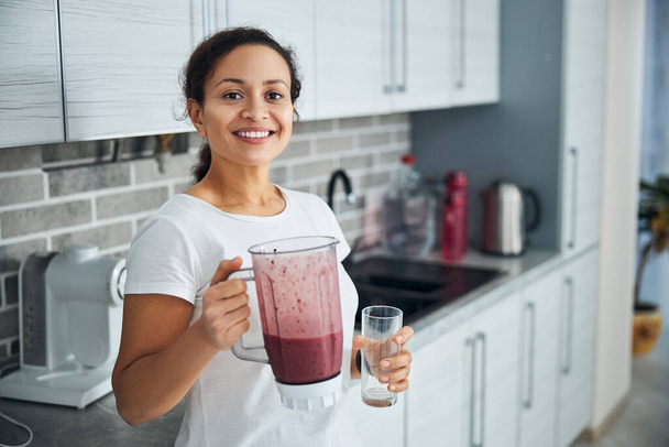 Fröhliche Hausfrau mit Frucht-Smoothie, die in die Kamera lächelt - Foto, Bild