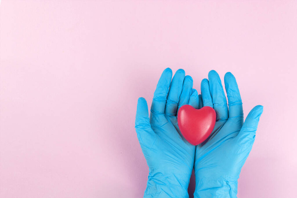 Hands in blue mediacl gloves holding heart shape, small heart in the safe hands of a doctor - 写真・画像