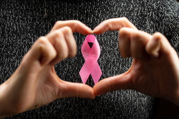 October Breast Cancer Awareness Month, an adult woman wearing a dark T-shirt with a pink ribbon in her hand to support people living and sick. International woman, mother and world cancer day concept. - Zdjęcie, obraz