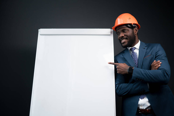 Portrait of an african american man in a suit standing next to a white magnetic board pointing his index finger at it - Foto, afbeelding