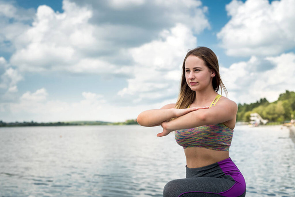  Krásný fitness trenér dělá jógu cvičení na protahování a flexibilitu v blízkosti jezera. zdravý životní styl - Fotografie, Obrázek