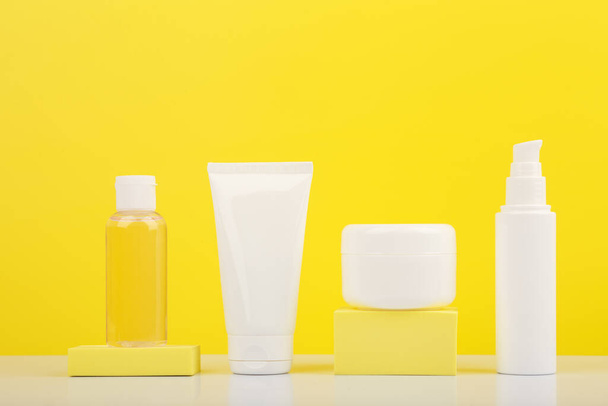 Set of cosmetic containers on white glossy table against bright yellow background.  - Zdjęcie, obraz