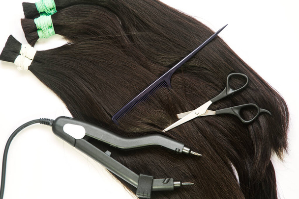 um grande fio de cabelo com um dispositivo fino de pente-tesoura para encapsular em um fundo branco. Foto de alta qualidade - Foto, Imagem