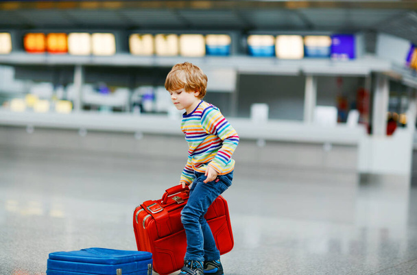 Happy little kid boy with big suitcase luggage at terminal on international airport. Preschool excited child wait for flight and going on vacations. Travel family lifestyle. - Фото, изображение