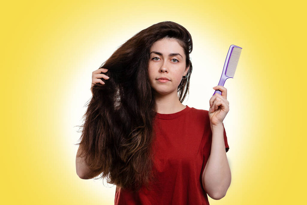 Porträt einer jungen kaukasischen Frau, die ihre dicken dunklen Haare zum Kämmen hält. Weißer Hintergrund. Haarpflegekonzept. - Foto, Bild