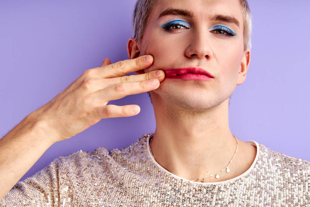 transvestite man smears lipstick on his cheek - Фото, зображення