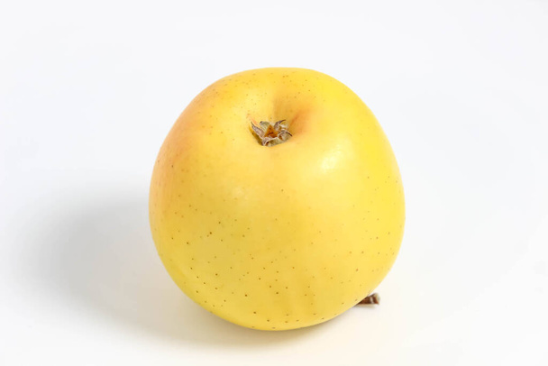 Ein gelber ganzer Apfel liegt kopfüber auf weißem Grund. Nahaufnahme, selektive Aufnahme. - Foto, Bild