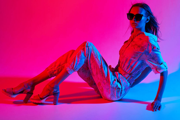 Fashion portrait of young elegant woman wearing overalls. Neon light - Photo, Image