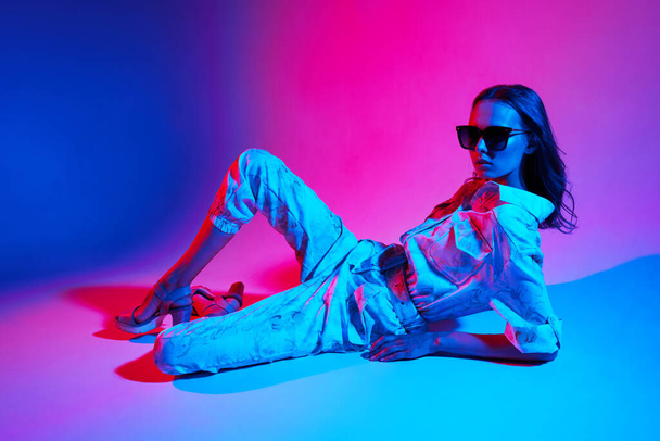 Fashion portrait of young elegant woman wearing overalls. Neon light - 写真・画像