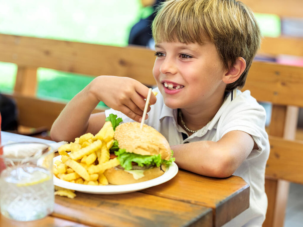 Leckere Hamburger mit Pommes, die ein Kind an einem sonnigen Tag isst. - Foto, Bild