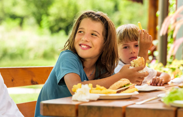 Ízletes hamburger sült krumplival, amit egy gyerek eszik egy napsütéses napon.. - Fotó, kép