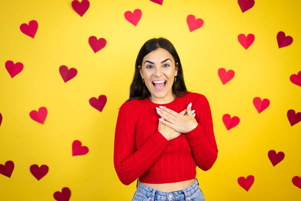 Young caucasian woman over yellow background with red hearts smiling with her hands on her chest and grateful gesture on her face. - 写真・画像