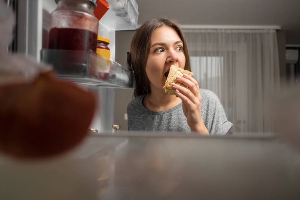 young woman looks into the fridge, view from fridge, girl eating at night, fears - 写真・画像