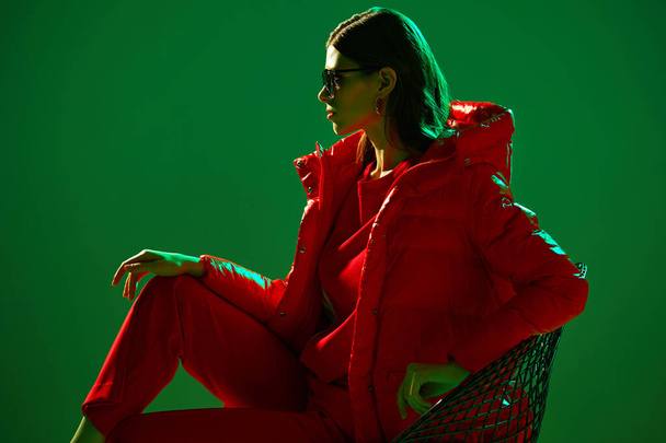 Fashion portrait of elegant trendy woman in red down jacket. Neon light, sunglasses, studio shot - Foto, immagini