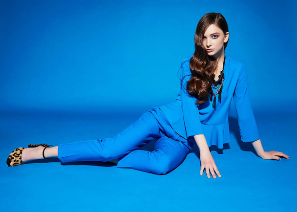 High fashion portrait of young elegant woman. Blue blouse, blue pants, curly hair, leopard shoes. Blue background - Valokuva, kuva
